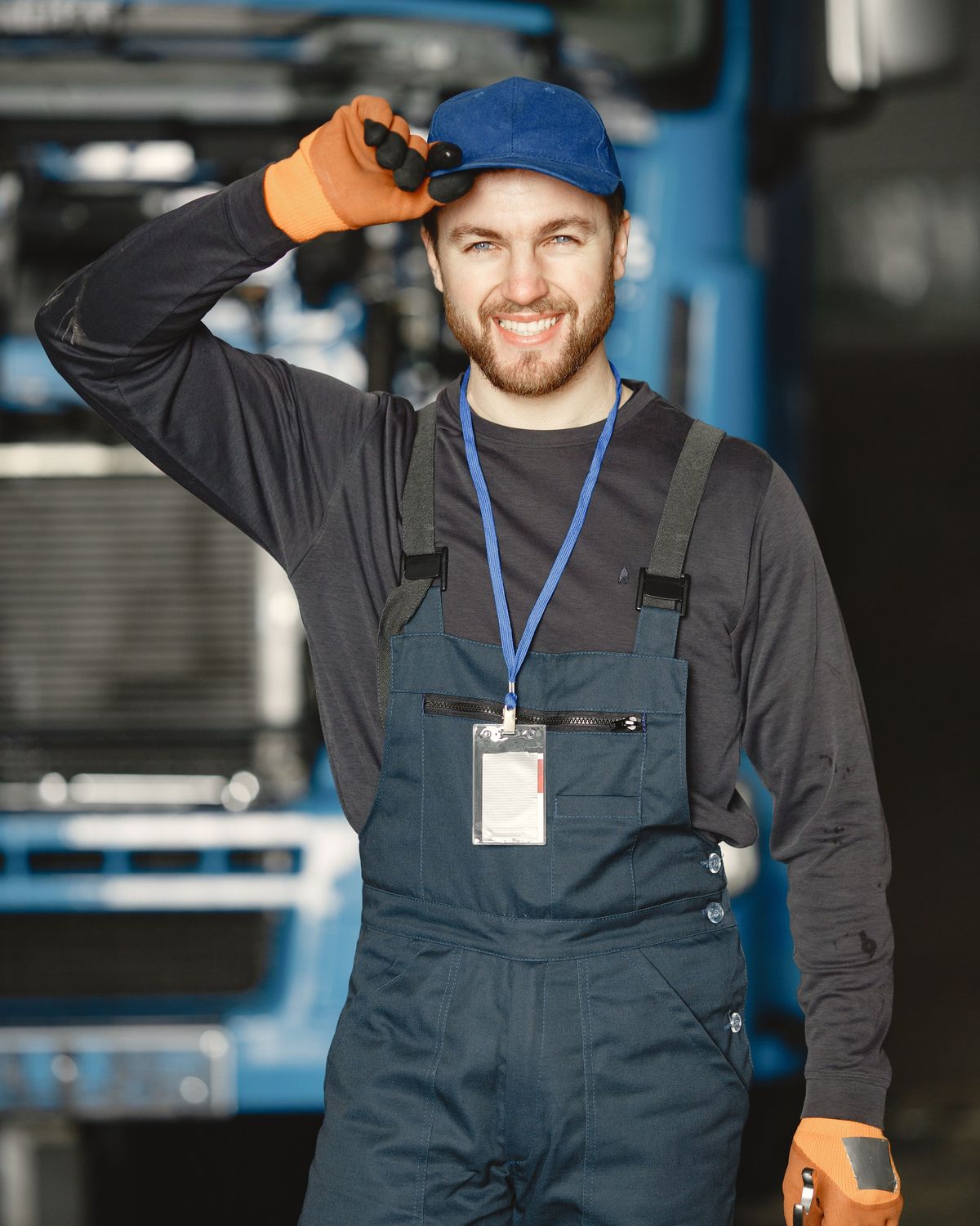 Smiling diesel mechanic in work overalls and gloves in front of a truck